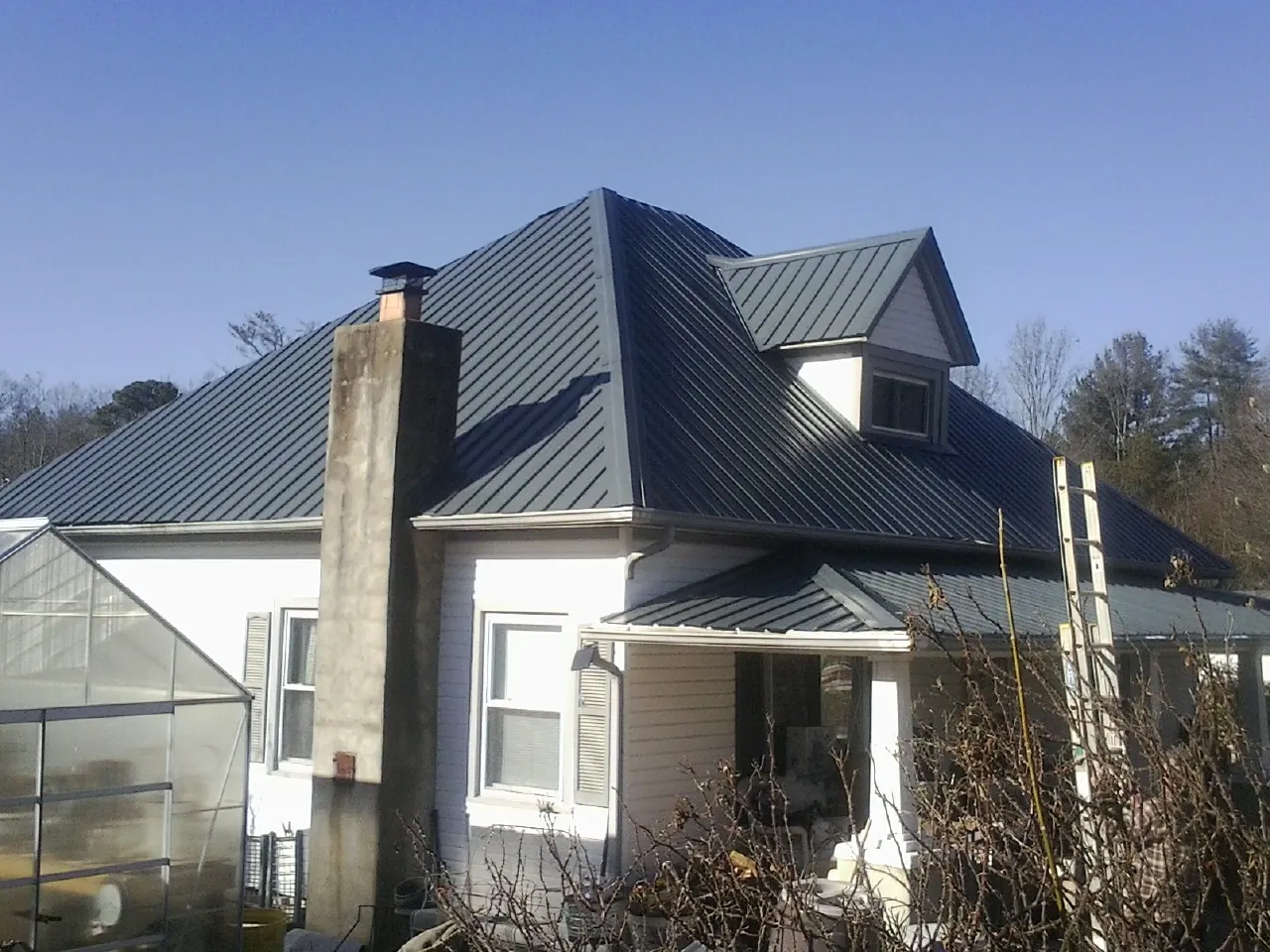Dark blue standing seam metal roof on a white farmhouse with dormer — Slate & Tile Roof Repair by Roofing Brothers in Romulus
