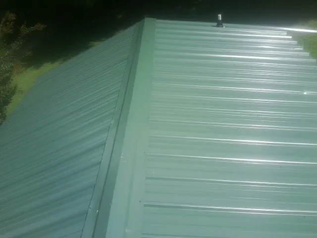 New green metal panels meeting at the ridge of a roof — Flat Roof Repair work by our crew in Romulus