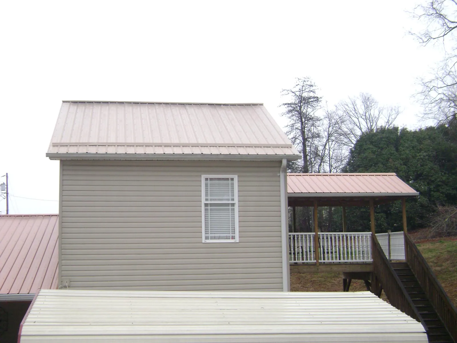 Tan metal roofs on a two story addition and attached porch, from a Roof Replacement job in Romulus